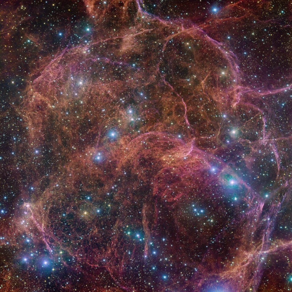 Bright blue stars in front of a background of colorful filaments of gas and dust